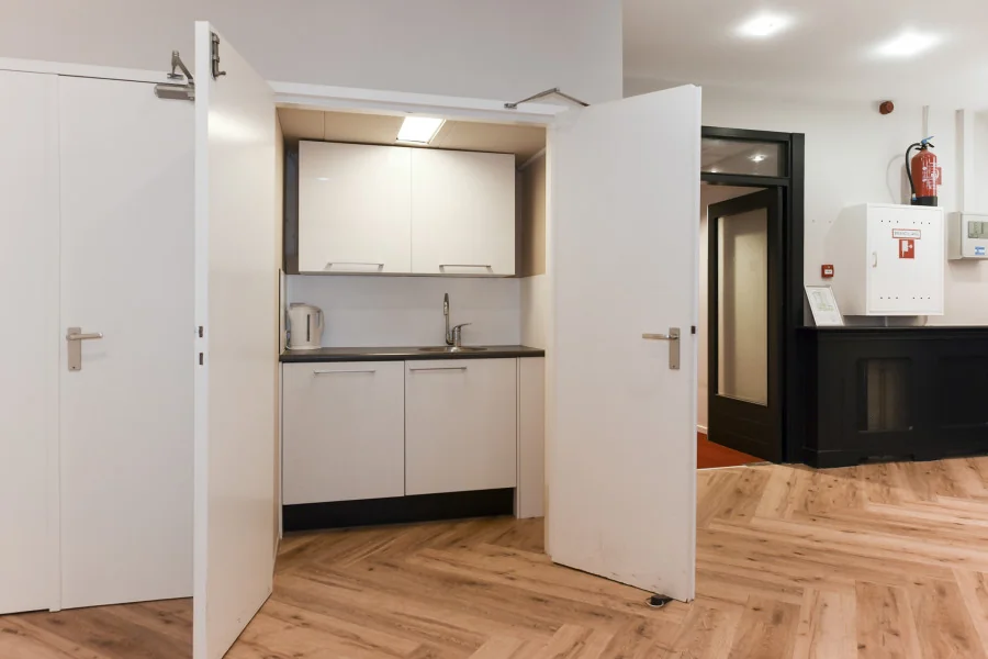 Kleine kitchenette met witte kastjes en gootsteen in een kantoorruimte aan het Sweelinckplein 9-21 in Den Haag.