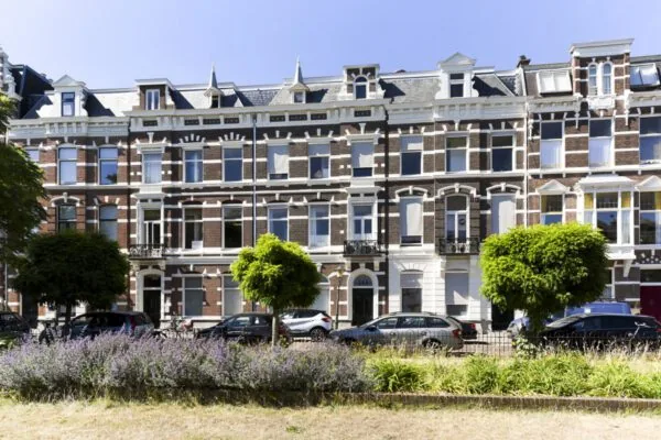 Voorgevel van een klassiek herenhuis aan het Sweelinckplein in Den Haag met geparkeerde auto's en groenstrook op de voorgrond.