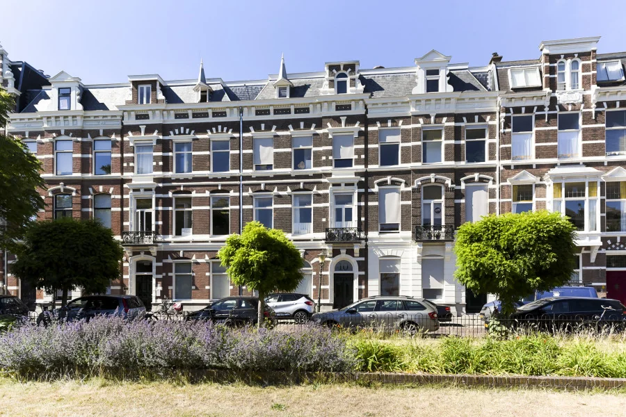Voorgevel van een klassiek herenhuis aan het Sweelinckplein in Den Haag met geparkeerde auto's en groenstrook op de voorgrond.