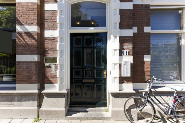 Voordeur van een kantoorruimte aan het Sweelinckplein 9-11 in Den Haag met rode bakstenen gevel en geparkeerde fiets.