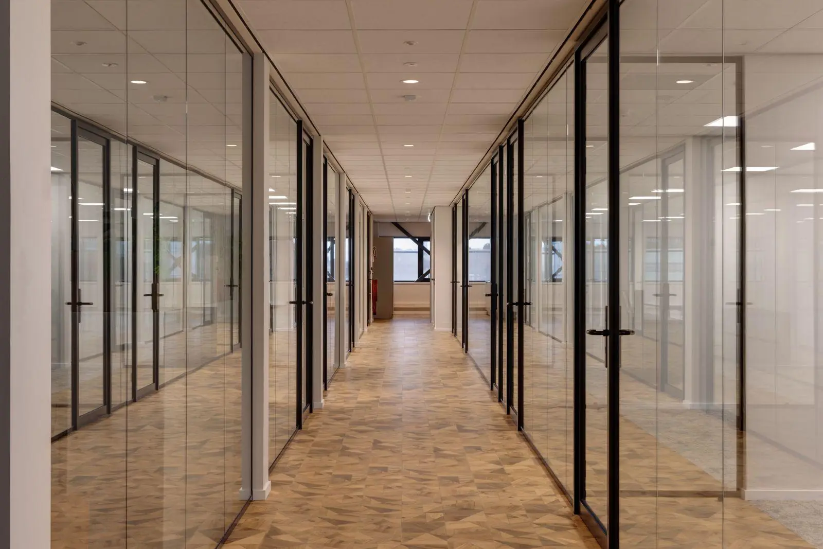 Gang met glazen kantoorwanden en houten vloer in bedrijfsgebouw aan de Vanadiumweg 11 in Amersfoort.