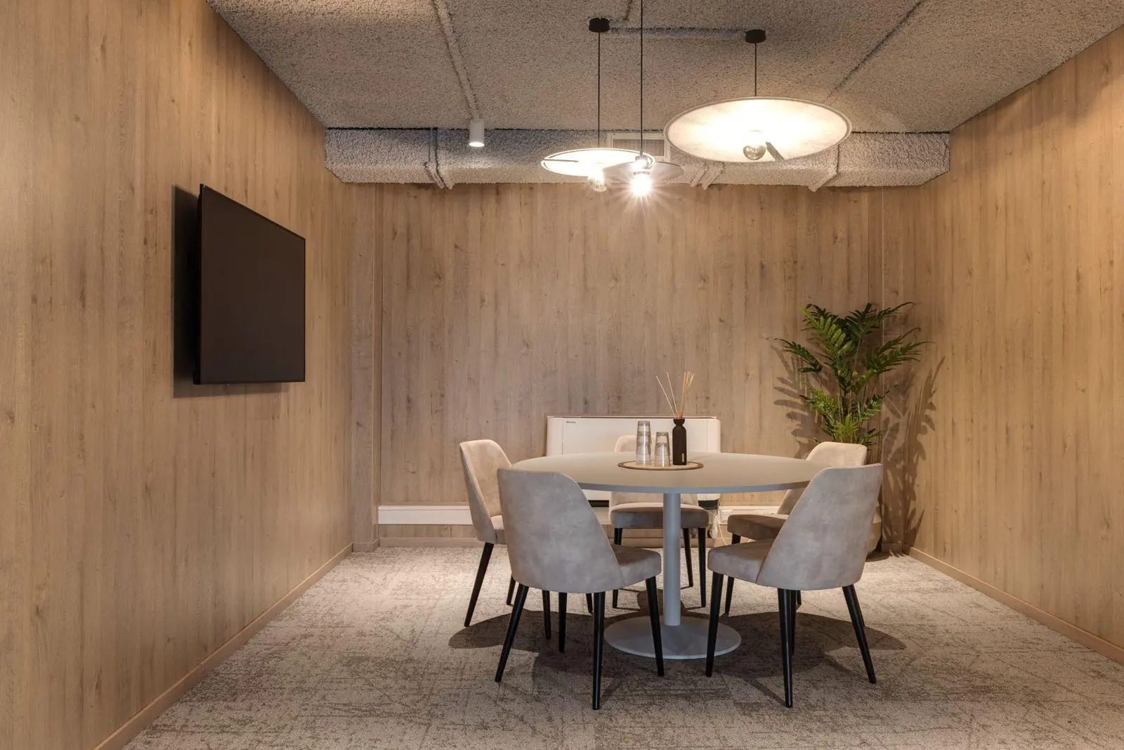 Vergaderruimte met ronde tafel, vier stoelen, wandtelevisie en een plant in een modern kantoor aan de Vanadiumweg 11 in Amersfoort.