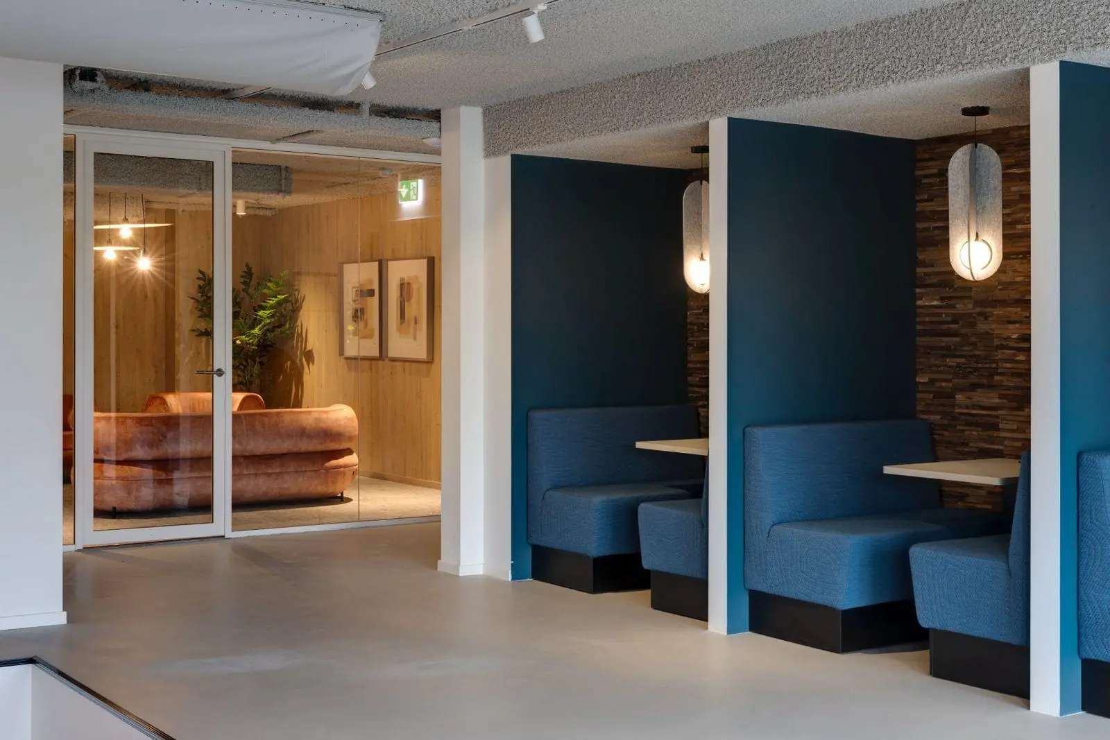 Moderne kantoorruimte aan de Vanadiumweg 11 in Amersfoort met blauwe zithoeken en een glazen vergaderruimte met roze banken.