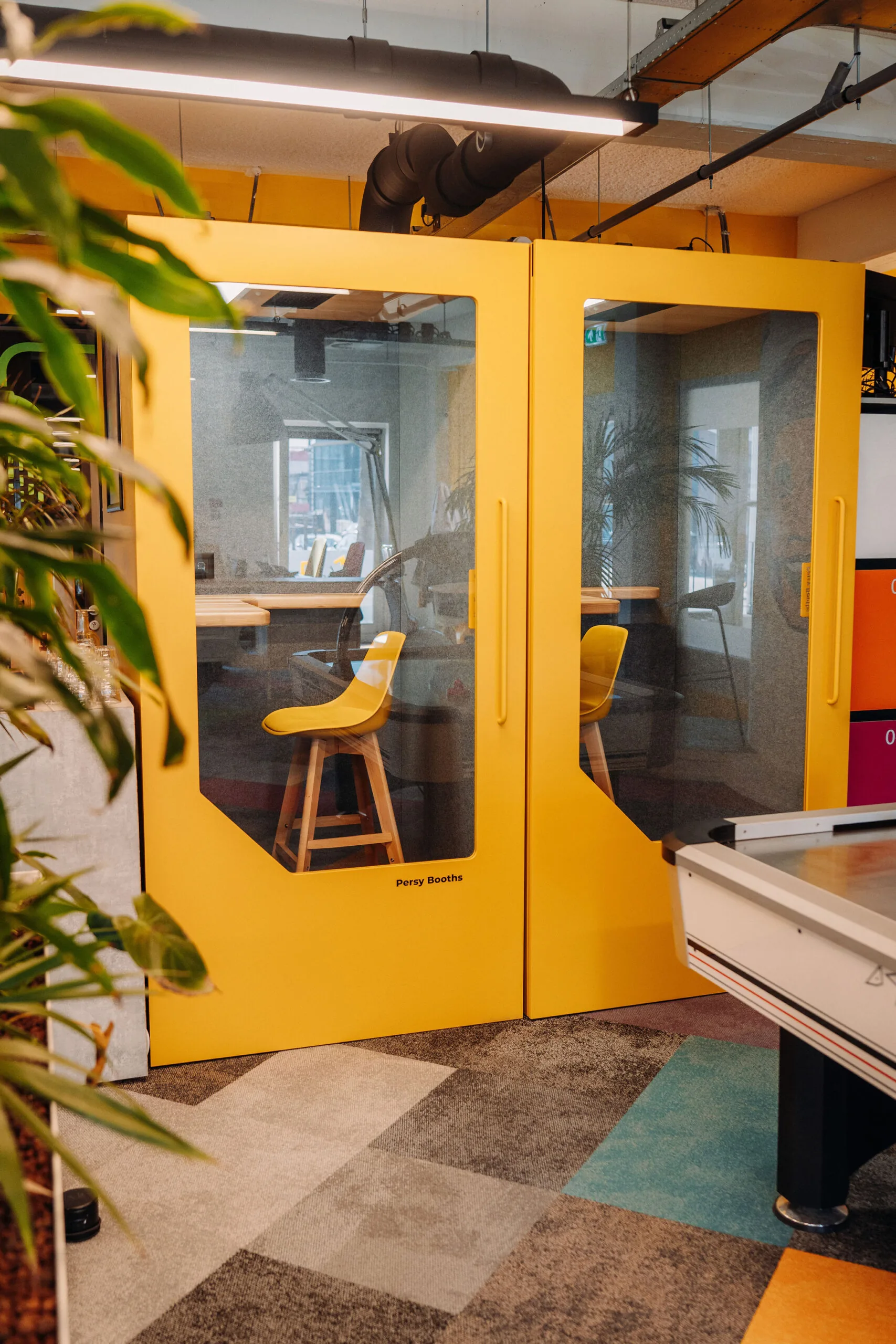 Gele vergaderruimte met glazen deuren en barkrukken in een kleurrijk kantoor aan de Willem Fenengastraat 16 in Amsterdam.