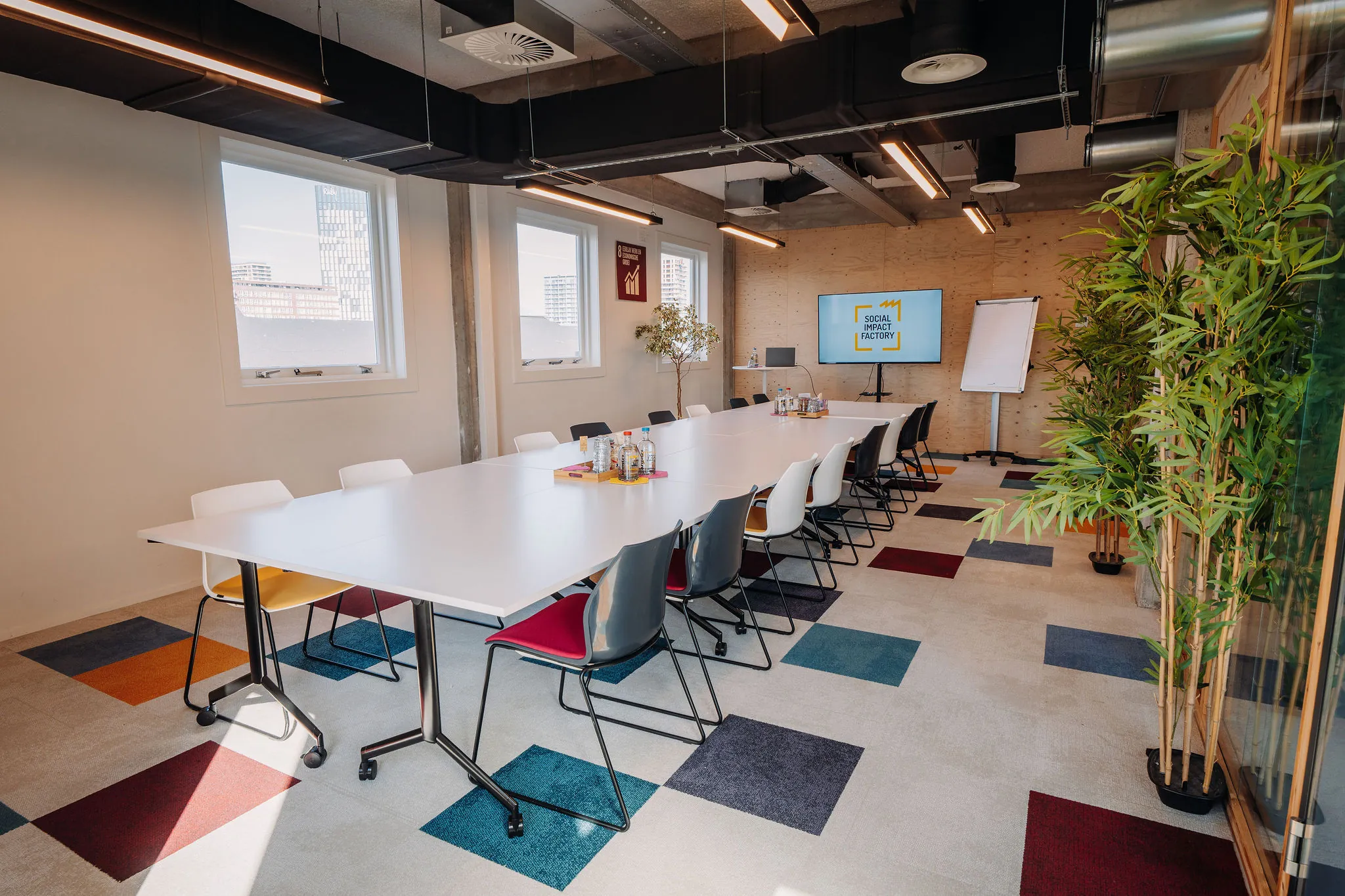 Moderne vergaderruimte aan de Willem Fenengastraat 17 in Amsterdam met lange tafel, kleurrijke stoelen en presentatiescherm.