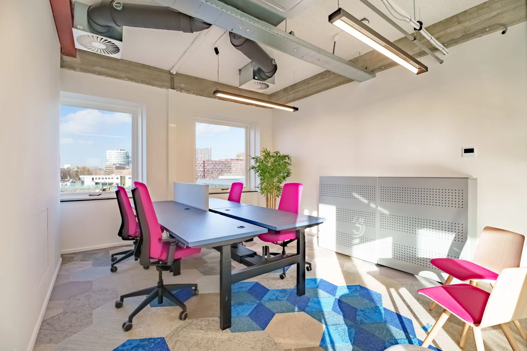 Moderne kantoorruimte met felroze bureaustoelen, dubbele werkplekken en uitzicht op de Willem Fenengastraat in Amsterdam.