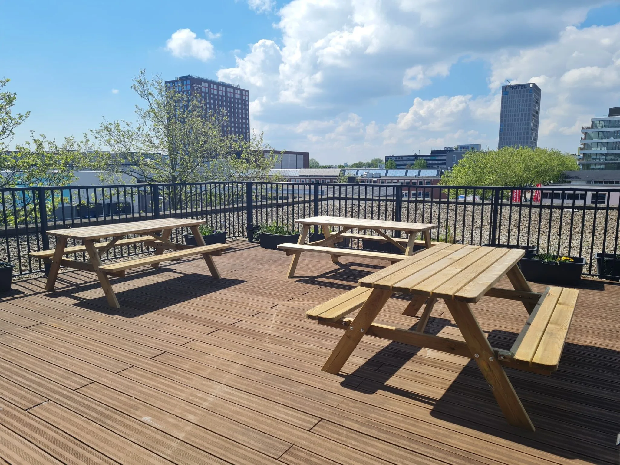 Houten picknicktafels op een zonnig dakterras aan de Willem Fenengastraat 2 in Amsterdam met uitzicht op kantoorpanden.