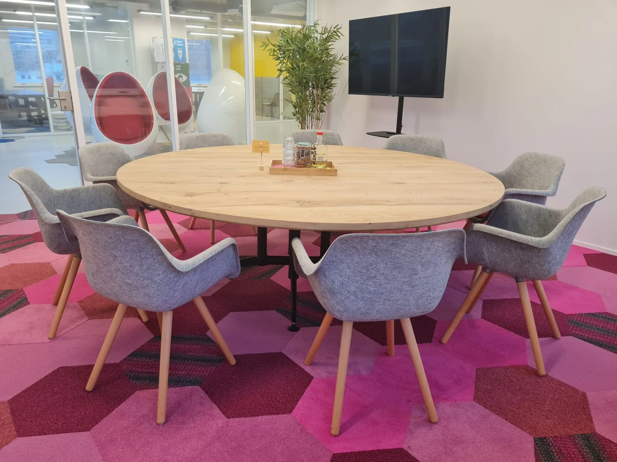 Vergaderruimte met ronde houten tafel, grijze stoelen en kleurrijk roze tapijt in een modern kantoor aan de Willem Fenengastraat in Amsterdam.