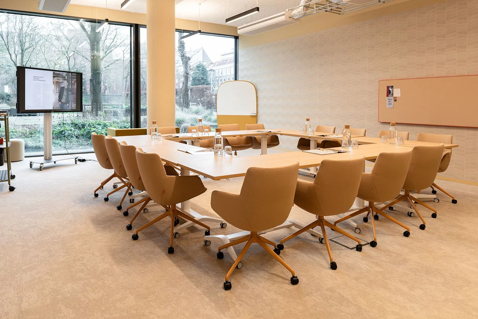 Moderne vergaderruimte aan de Zeestraat 70 in Den Haag met beige stoelen, een grote tafel en een presentatiescherm.
