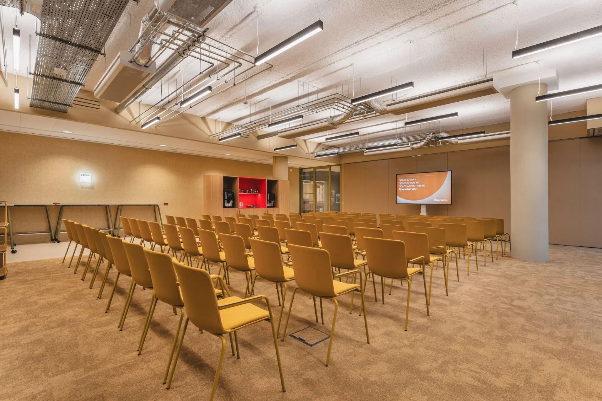 Vergaderruimte met opgestelde stoelen, presentatiescherm en koffiecorner in kantoorpand aan de Zeestraat 70 in Den Haag.