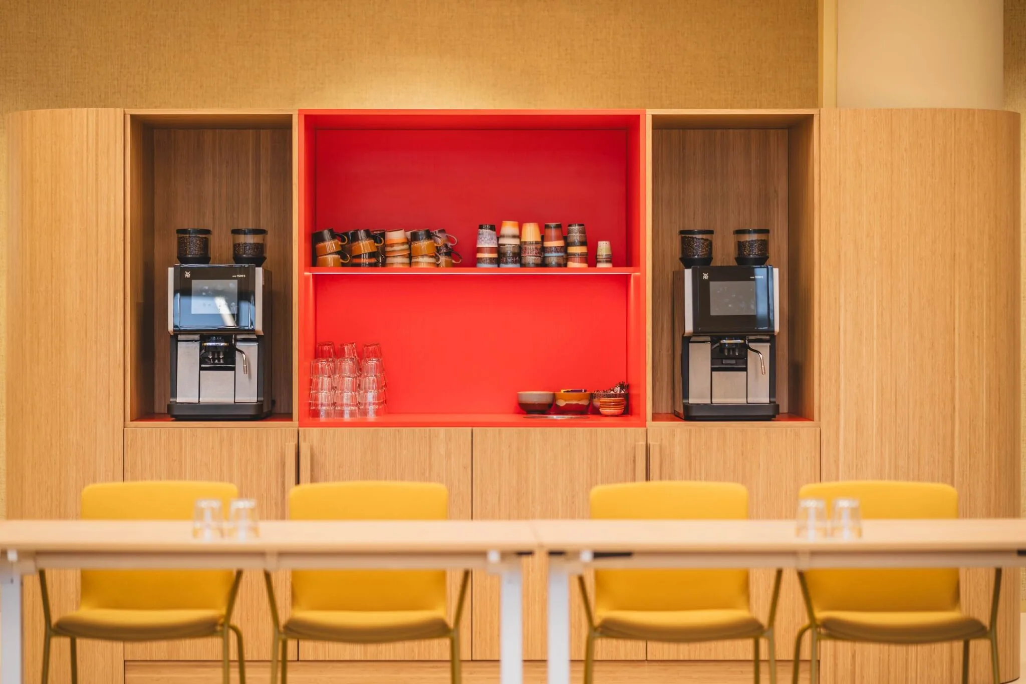 Koffiehoek met twee koffiemachines, gekleurde mokken en glazen in een moderne kantoorruimte aan de Zeestraat 70 in Den Haag.