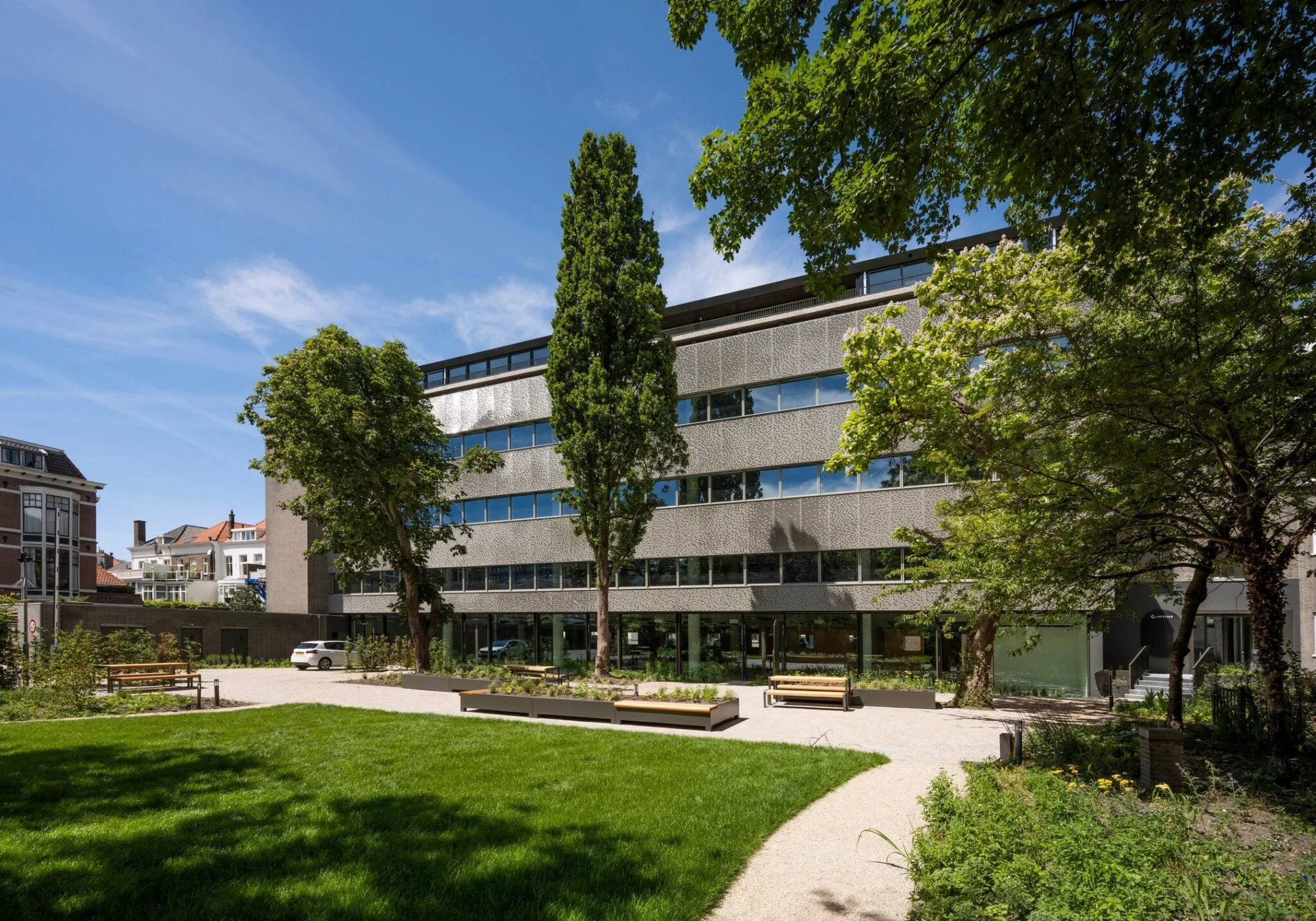 Modern kantoorgebouw aan de Zeestraat 70 in Den Haag met een groene voortuin en bankjes.