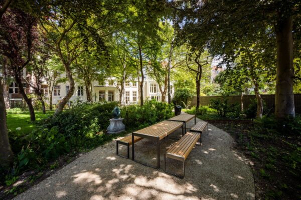 Groene tuin met zitbanken en kunstwerk achter het kantoorpand aan de Zeestraat 70 in Den Haag.