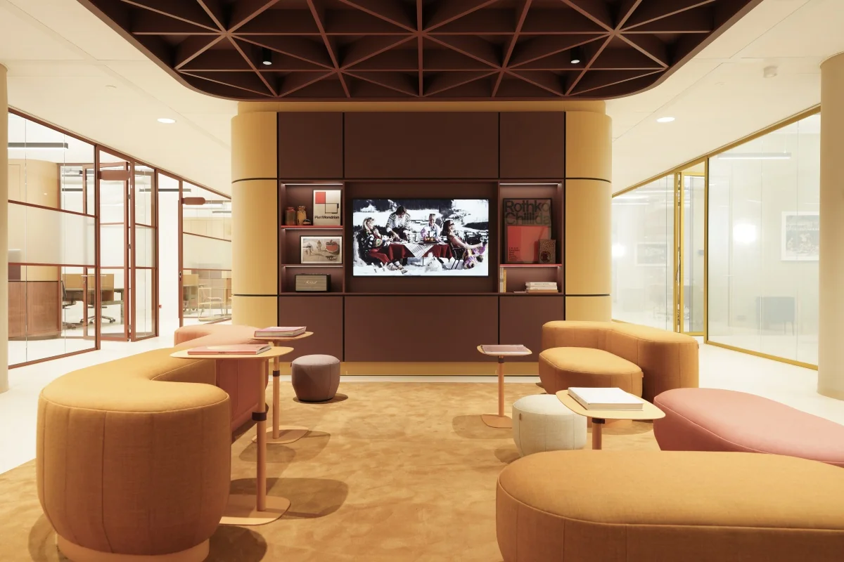 Moderne loungehoek in een stijlvolle kantoorruimte aan de Zeestraat 70 in Den Haag met kleurrijke zitbanken, een tv-scherm en glazen vergaderruimtes op de achtergrond.