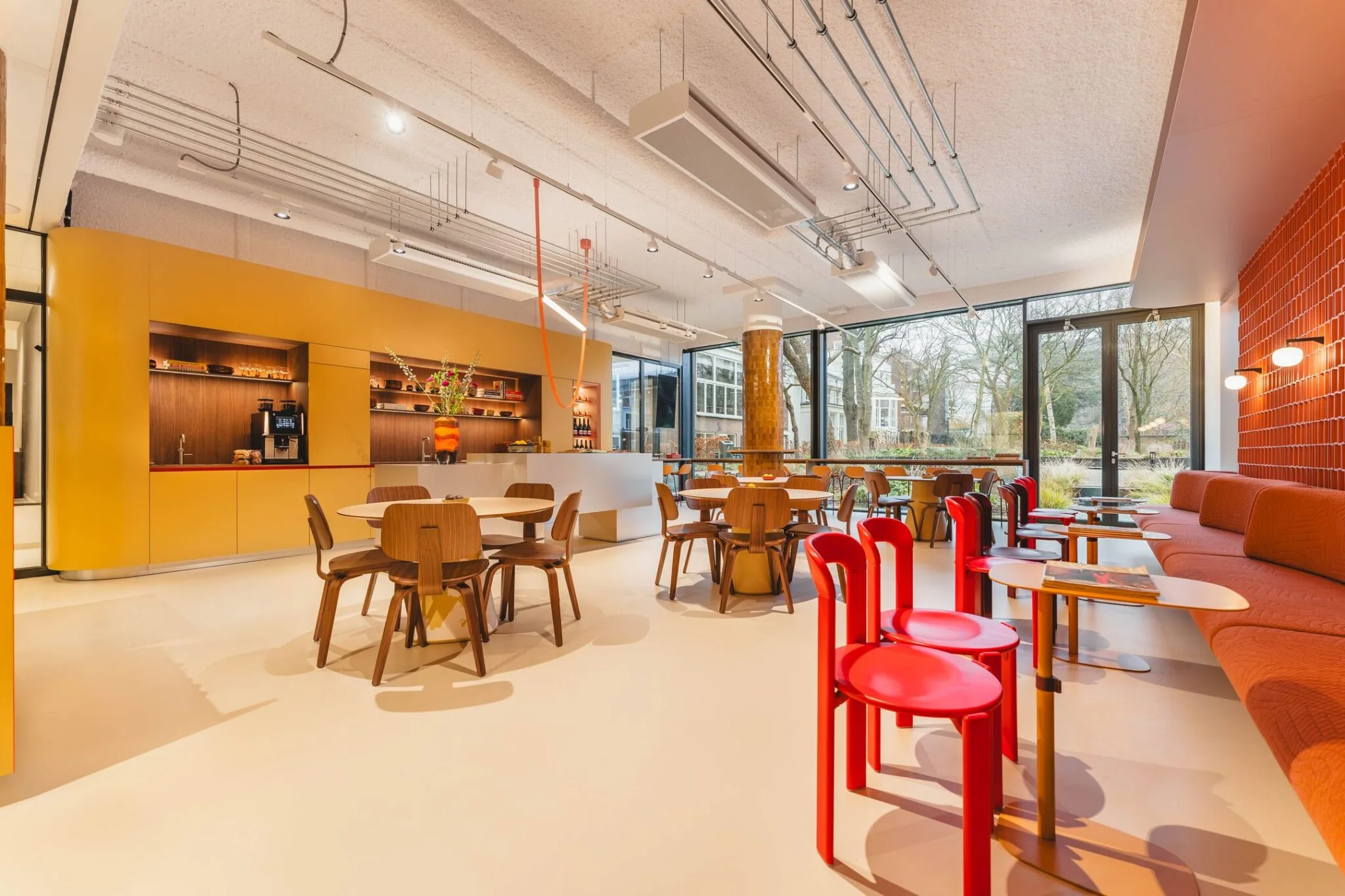 Moderne en kleurrijke kantoorruimte aan de Zeestraat 70 in Den Haag met zithoeken, een bar en grote ramen met uitzicht op een groene omgeving.