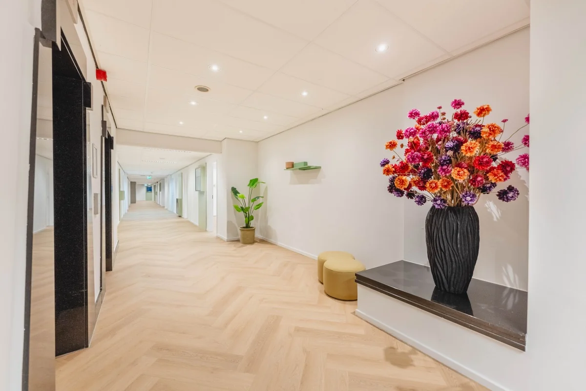 Modern ingerichte gang van kantoorpand Weesperstraat 107 met houten vloer, kleurrijk bloemstuk en planten.