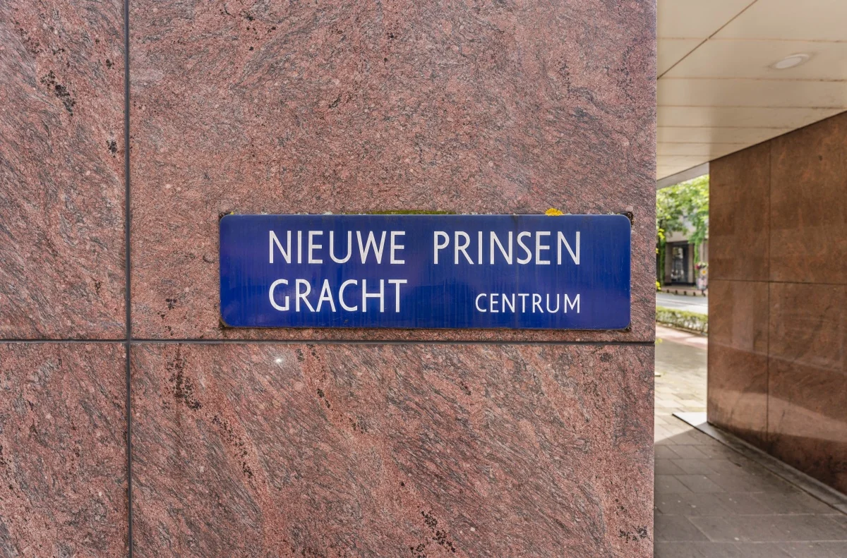 Straatnaambord met de tekst "Nieuwe Prinsengracht Centrum" bevestigd aan een roodbruine natuurstenen gevel.