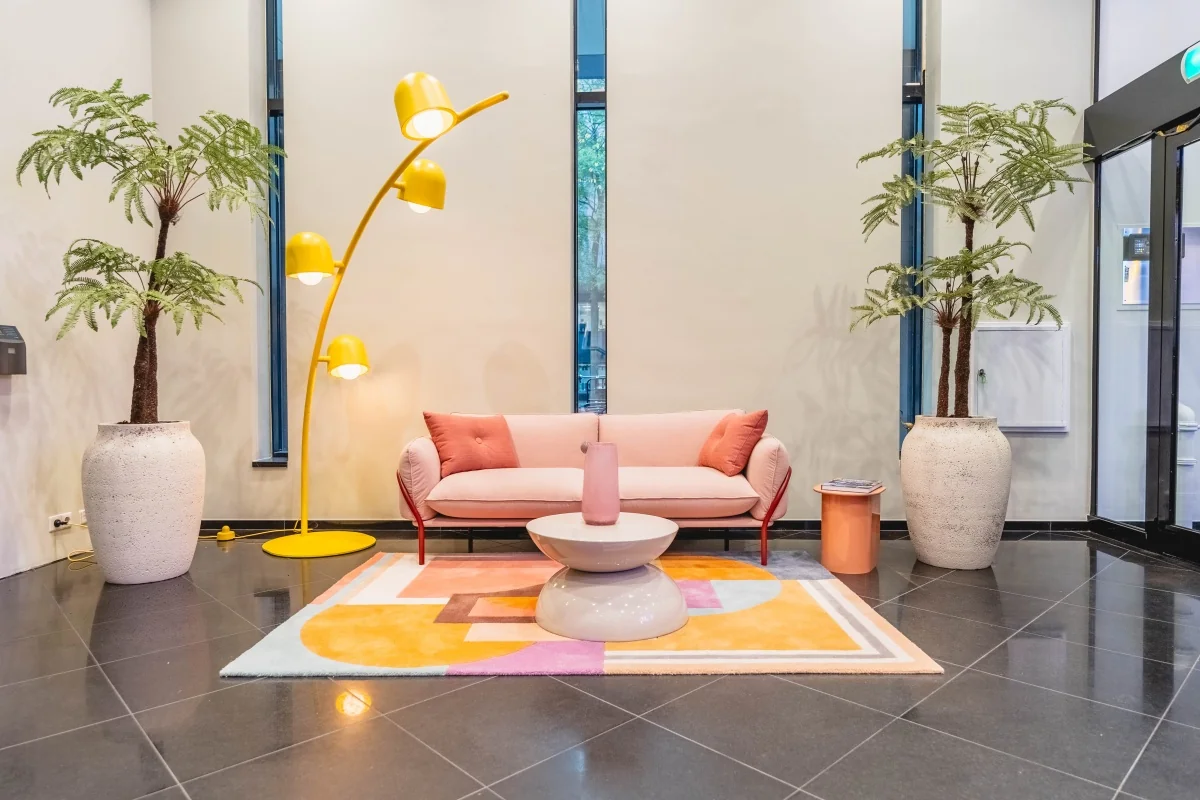 Moderne wachtruimte in kantoorgebouw Weesperstraat 107 met een roze bank, gele lamp, kleurrijk vloerkleed en grote planten.