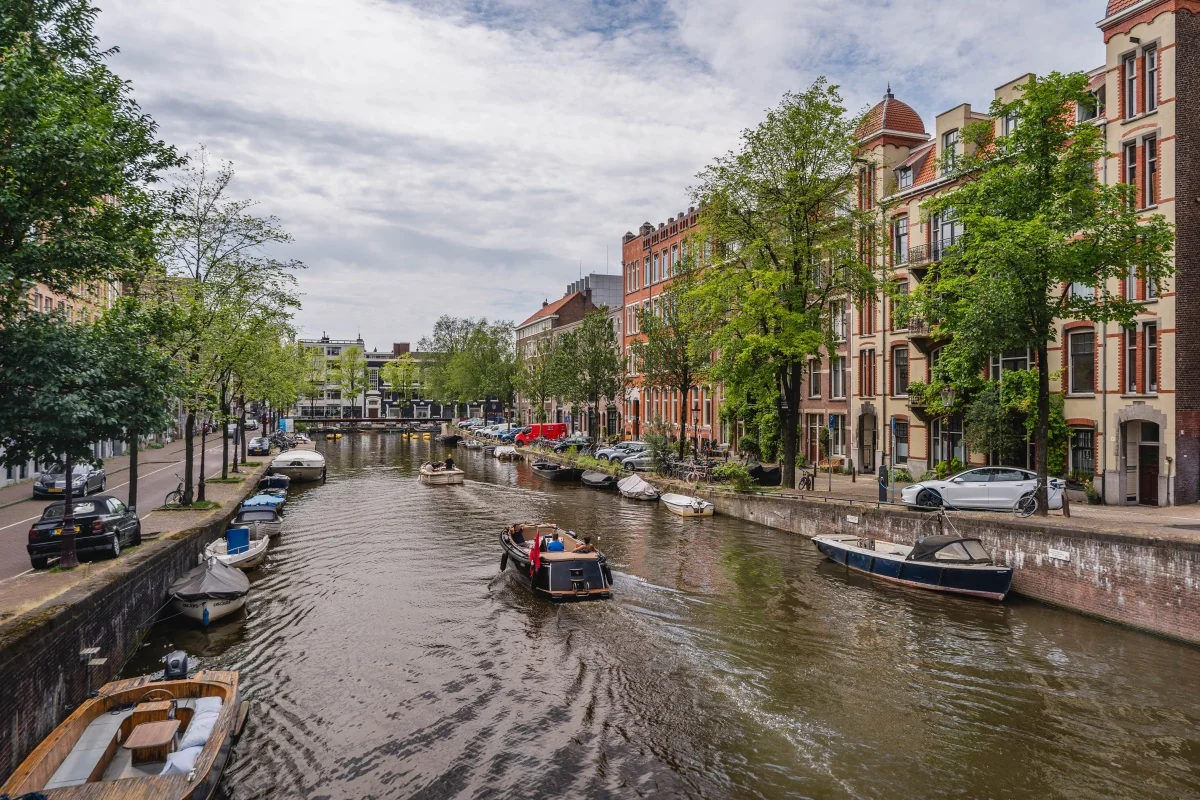 Grachtenpand met kantoorpanden aan de Weesperstraat 107 in Amsterdam, met boten op het water en bomen langs de kade.