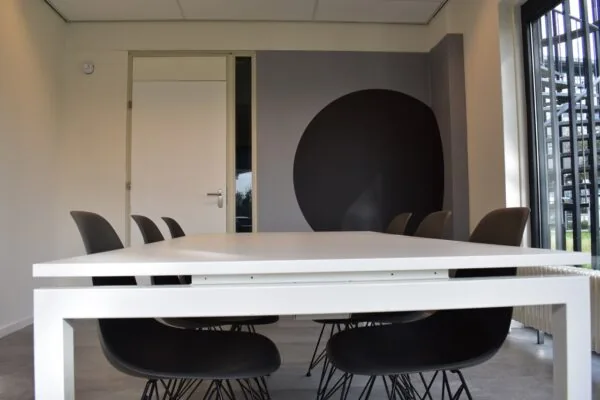 Moderne vergaderruimte aan de Keulenstraat 9 in Deventer met witte tafel, zwarte stoelen en grote ronde muurschildering.