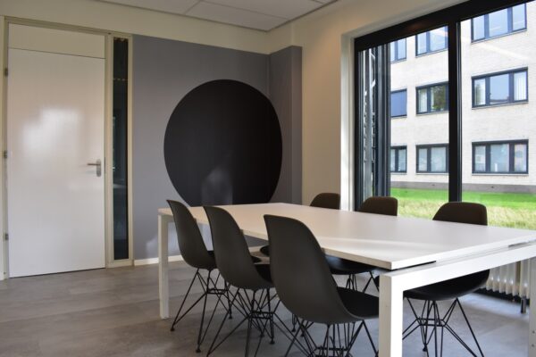 Moderne vergaderruimte aan de Keulenstraat 9 in Deventer met witte tafel, zwarte stoelen en grote ramen met uitzicht op kantooromgeving.
