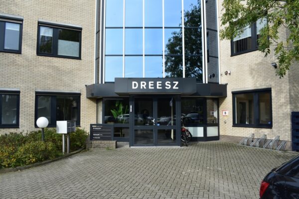 Ingang van kantoorgebouw DREESZ aan de Keulenstraat 9 in Deventer met parkeerplaatsen en fietsenrekken.