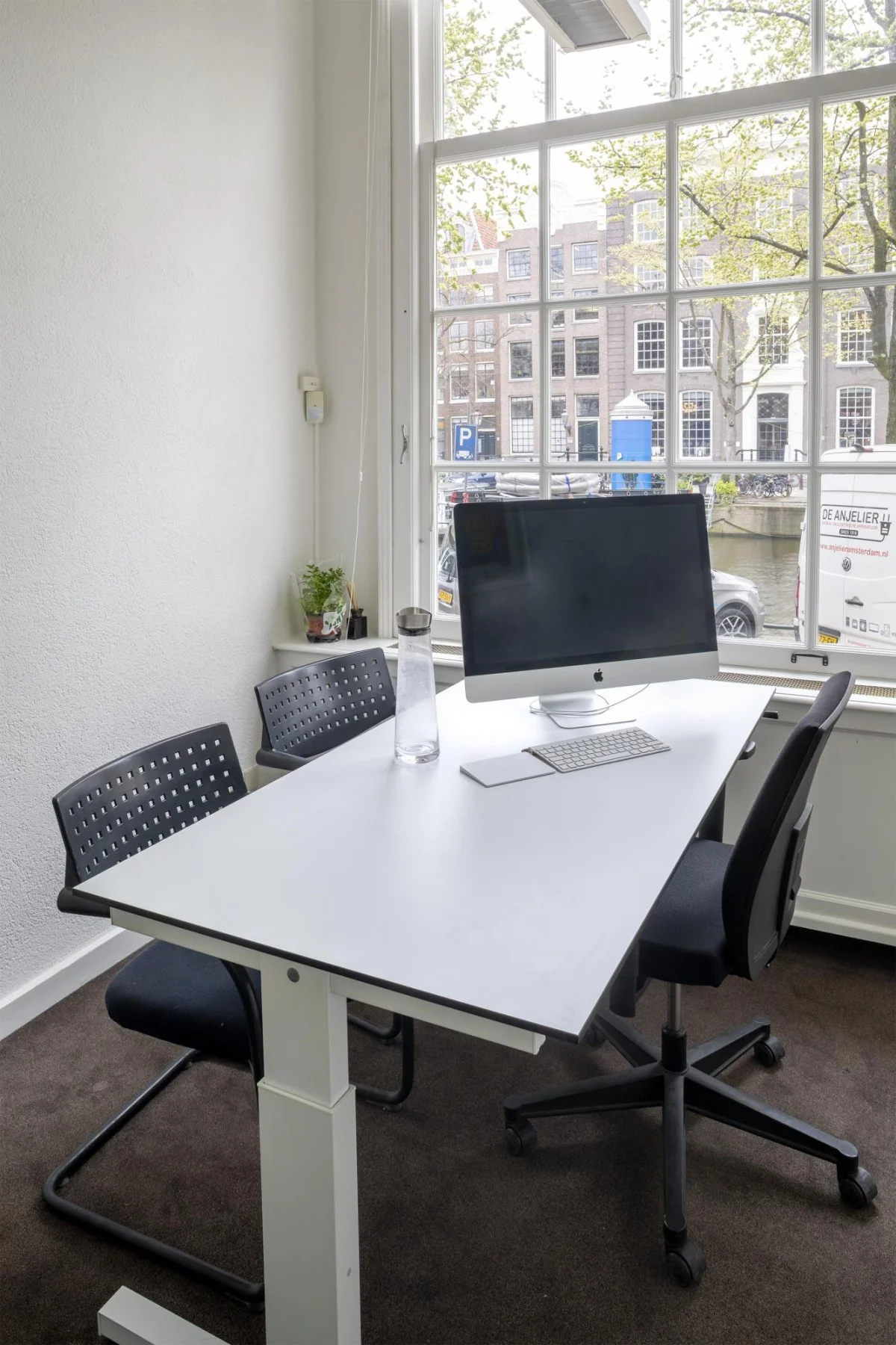 Modern kantoor met een bureau, iMac en uitzicht op de Keizersgracht in Amsterdam.