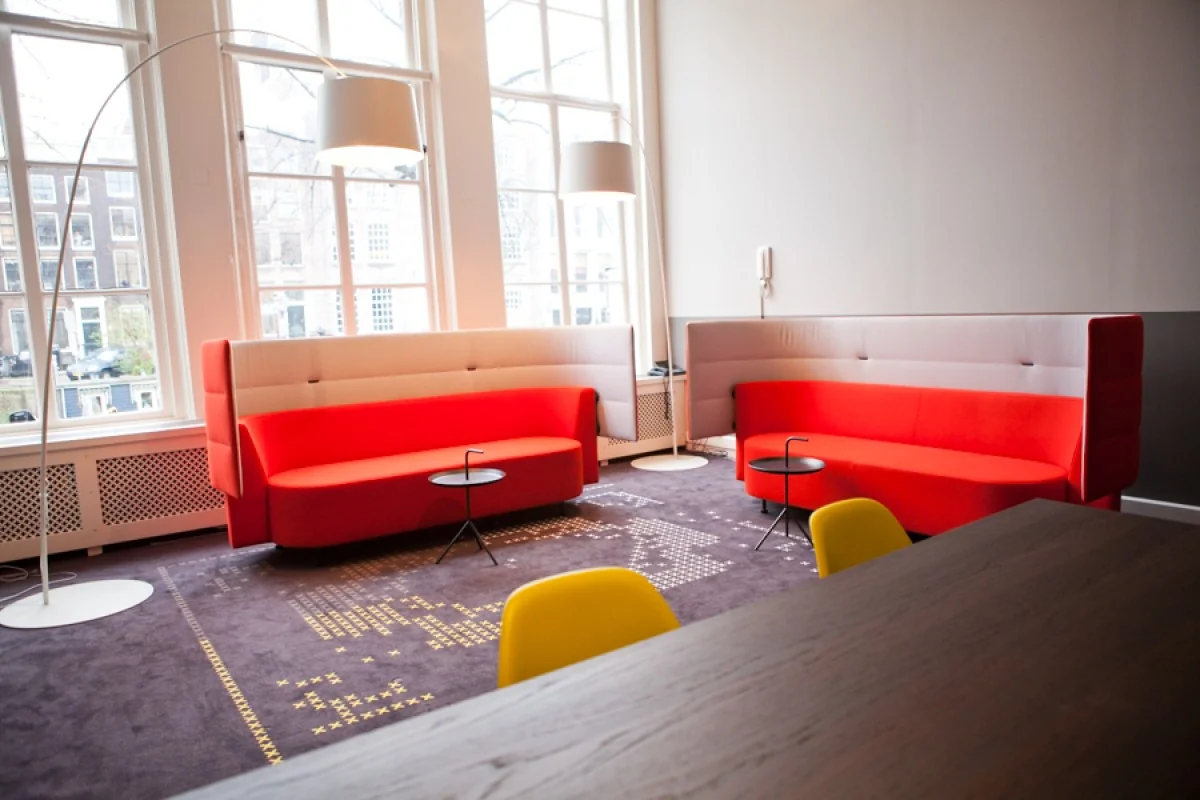 Moderne zithoek met rode en grijze banken, designlampen en grote ramen in een ruimte aan de Keizersgracht 106.