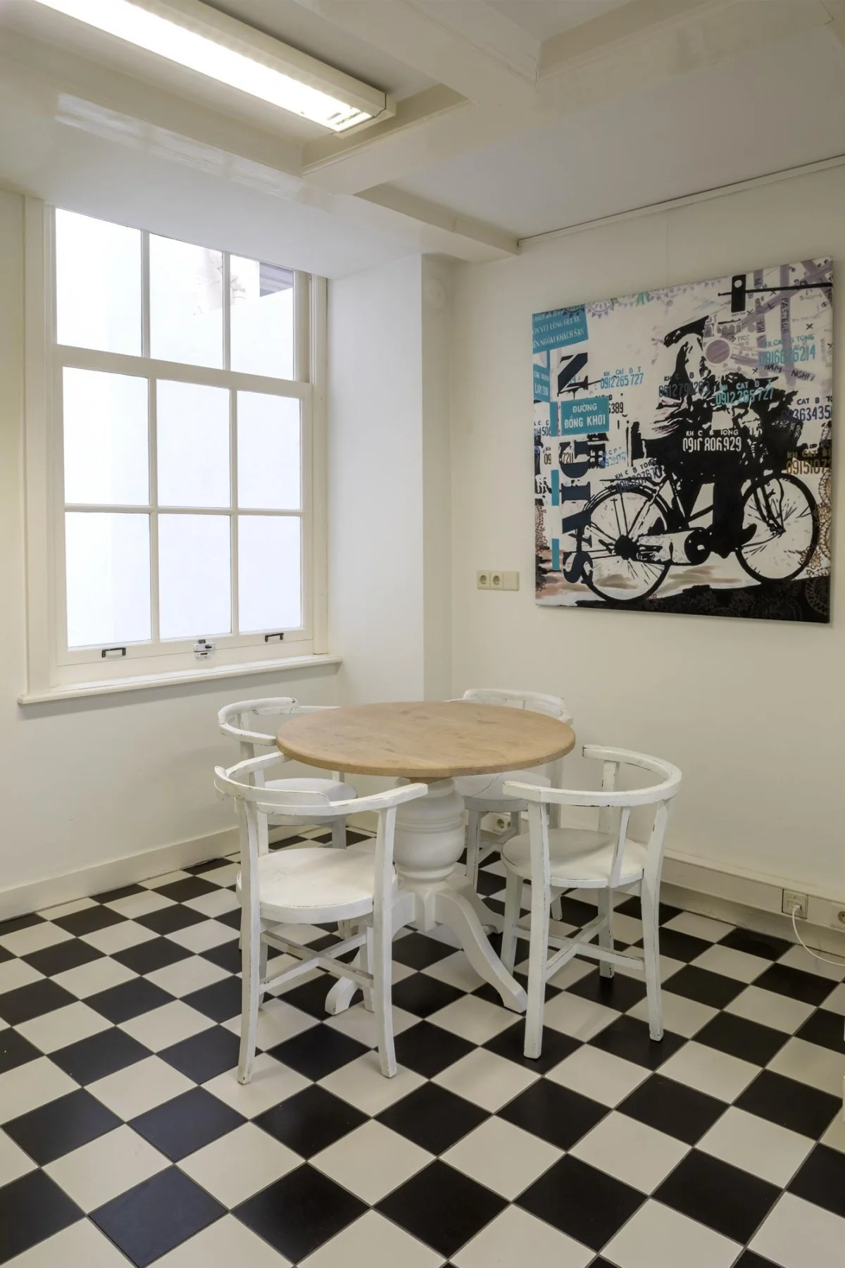 Kleine eetruimte met een rond houten tafelblad, vier witte stoelen, zwart-witte tegelvloer en een kunstwerk aan de muur in Keizersgracht 106.