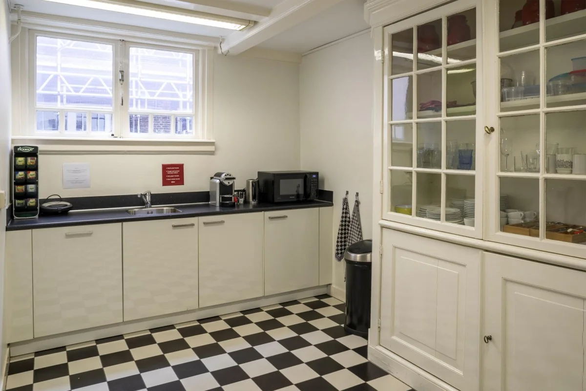 Kleine pantry met zwart-wit geblokte vloer, wit keukenblok, koffieautomaat en vitrinekast in Keizersgracht 106.