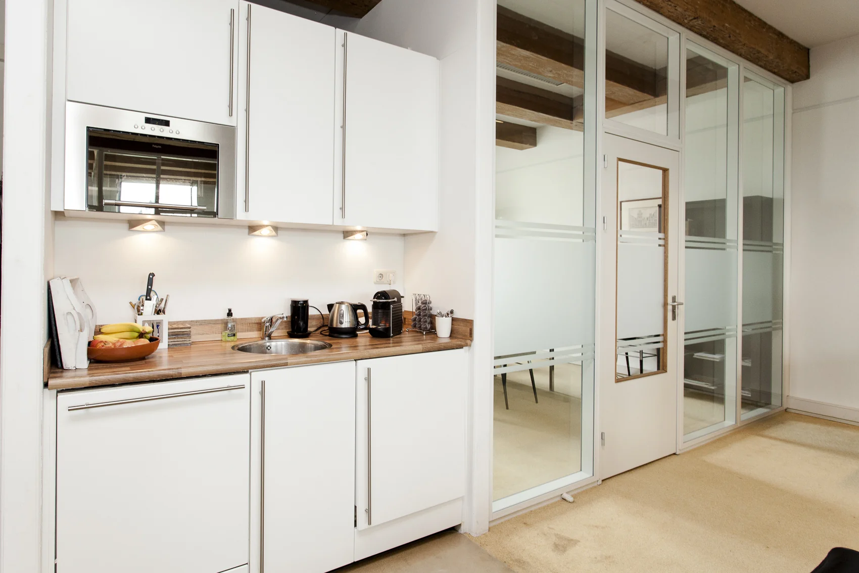 Moderne kitchenette in een kantoorruimte aan de Keizersgracht met witte kasten, houten werkblad en diverse keukenapparaten.