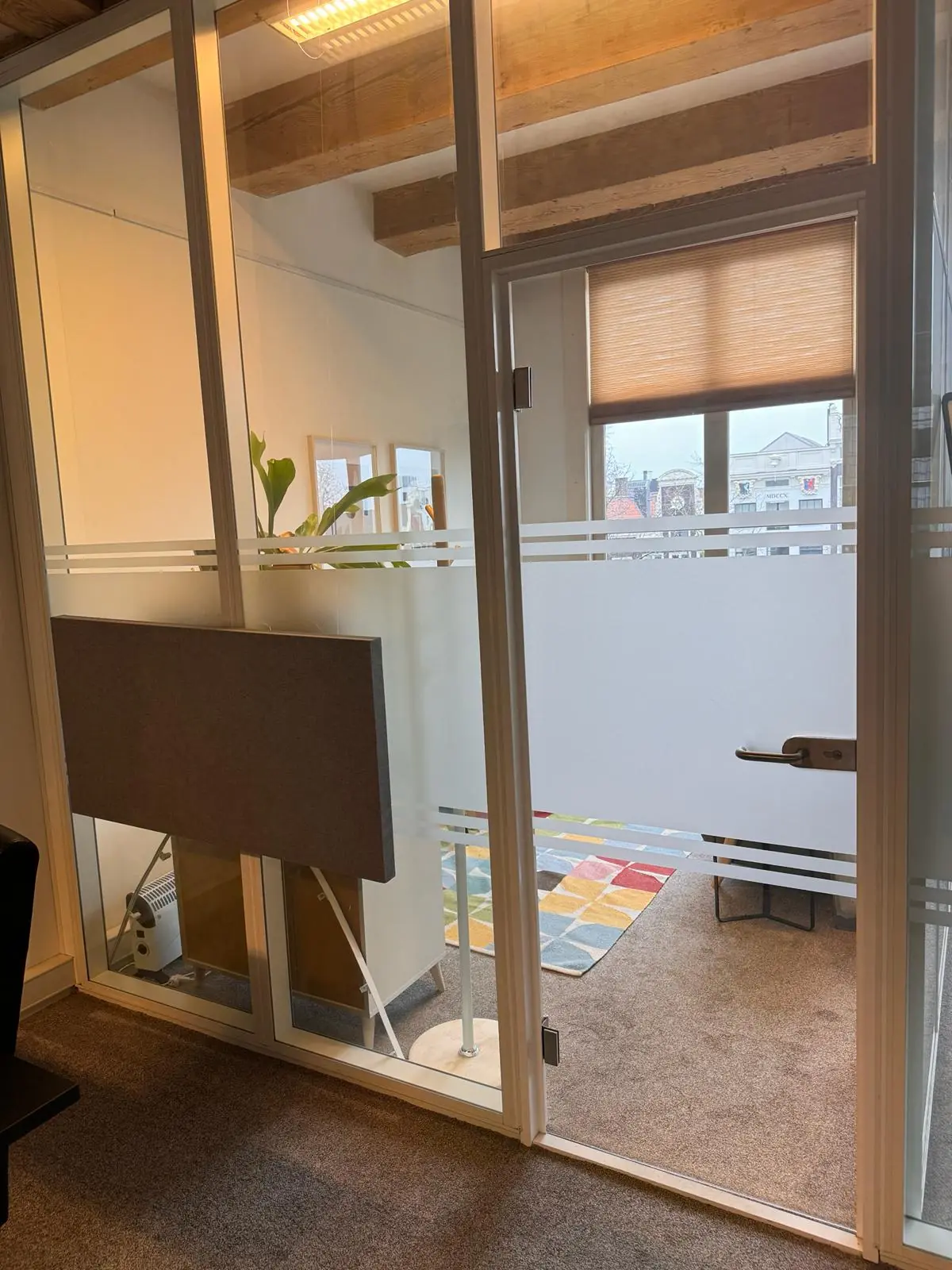 Glazen kantoorruimte aan de Keizersgracht 241 met vergezicht op klassieke gevels en een kleurrijk vloerkleed binnenin.
