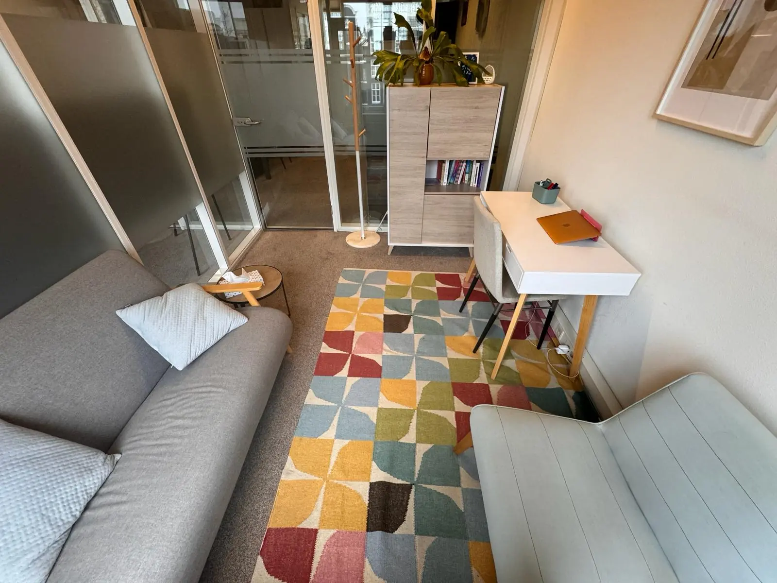 Kleine, modern ingerichte kantoorruimte aan de Keizersgracht 241 met een kleurrijk vloerkleed, zithoek en werktafel.
