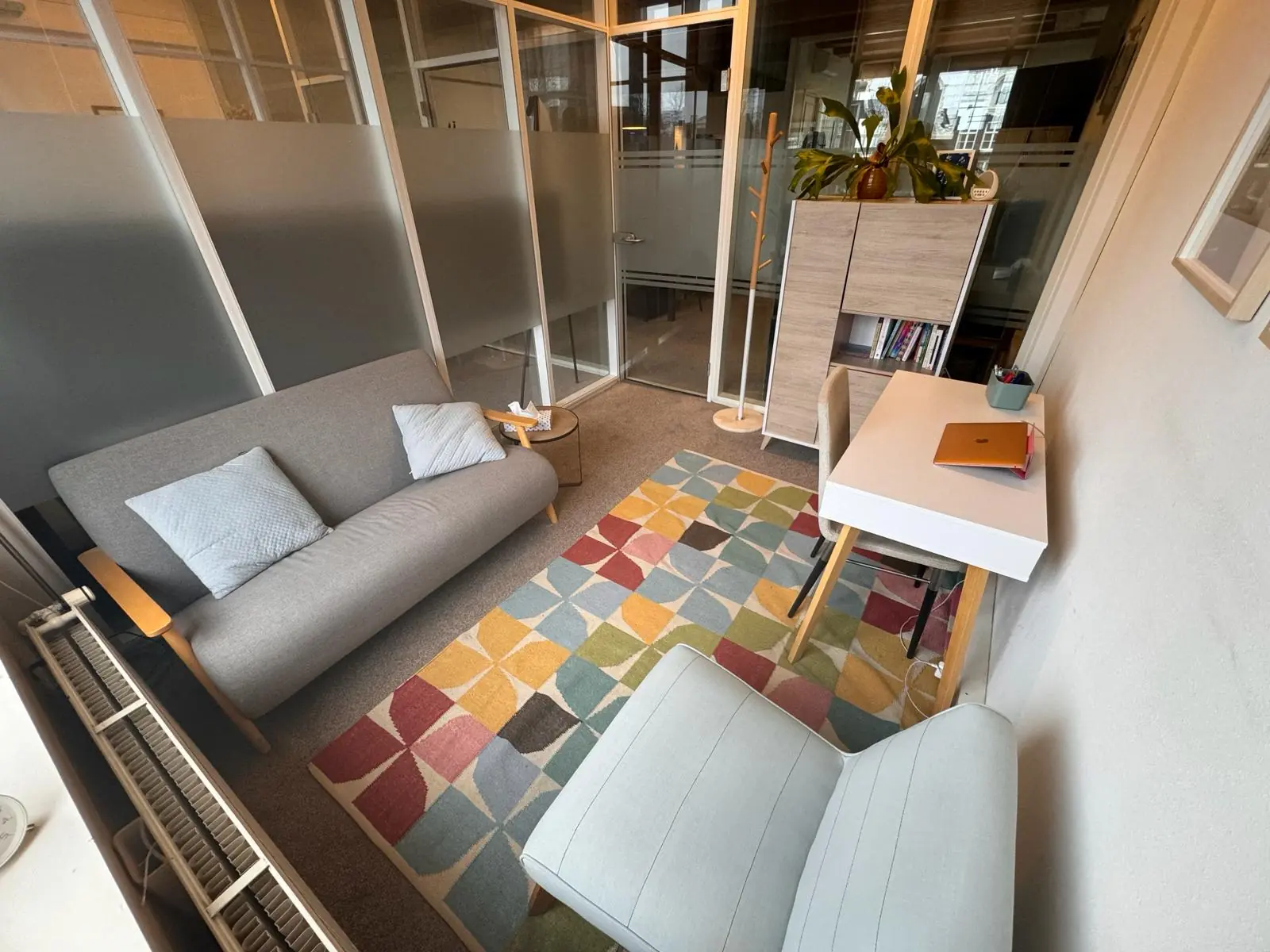 Kleine, moderne vergaderruimte aan de Keizersgracht 241 met een grijze bank, bureau, kleurrijk vloerkleed en glazen wanden.
