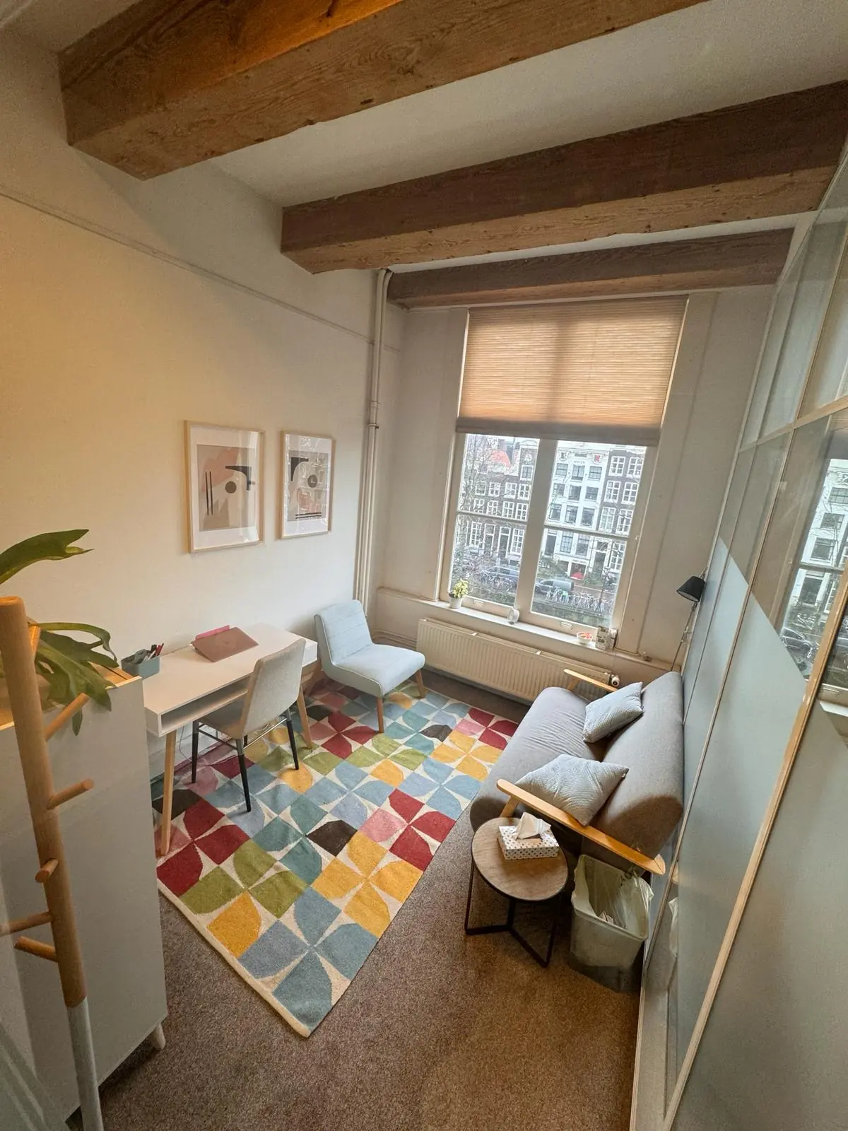 Kleine, sfeervolle werk- of gespreksruimte aan de Keizersgracht 241 met kleurrijk vloerkleed, bureau, bank en uitzicht op Amsterdamse grachtenpanden.
