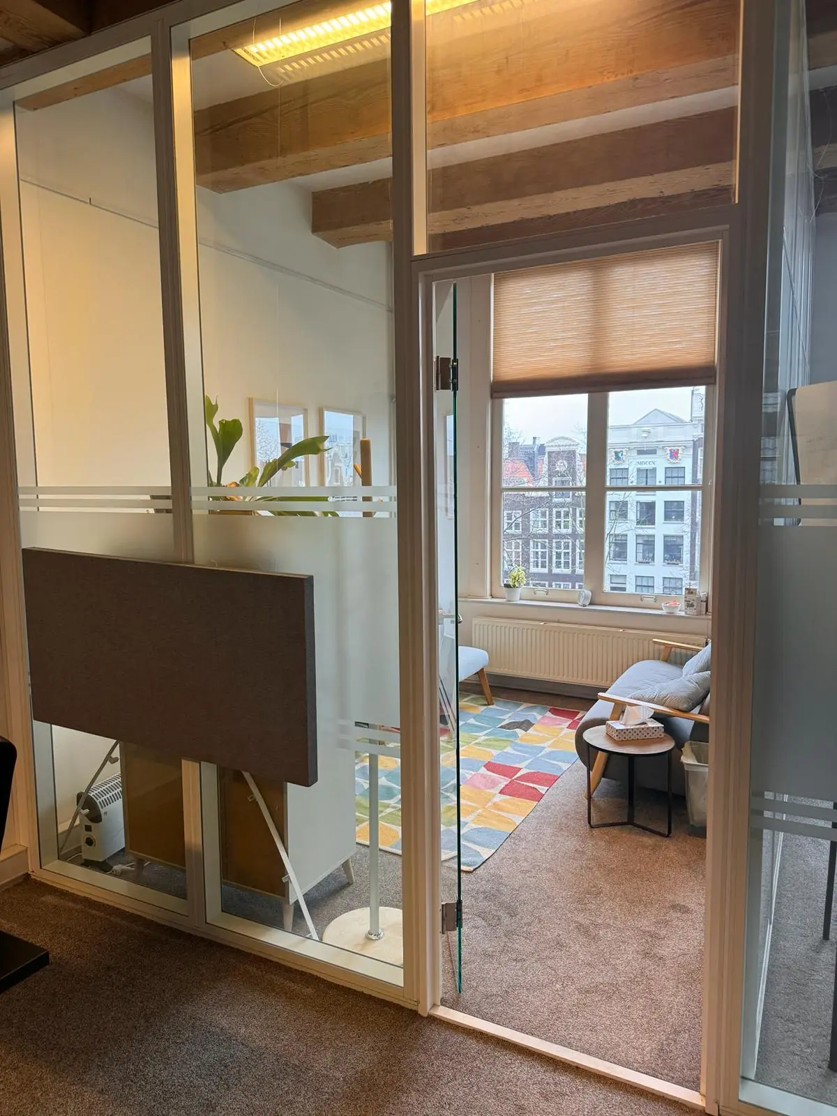 Kantoorruimte aan de Keizersgracht 241 met glazen wanden, een kleurrijk tapijt en uitzicht op de Amsterdamse grachtenpanden.