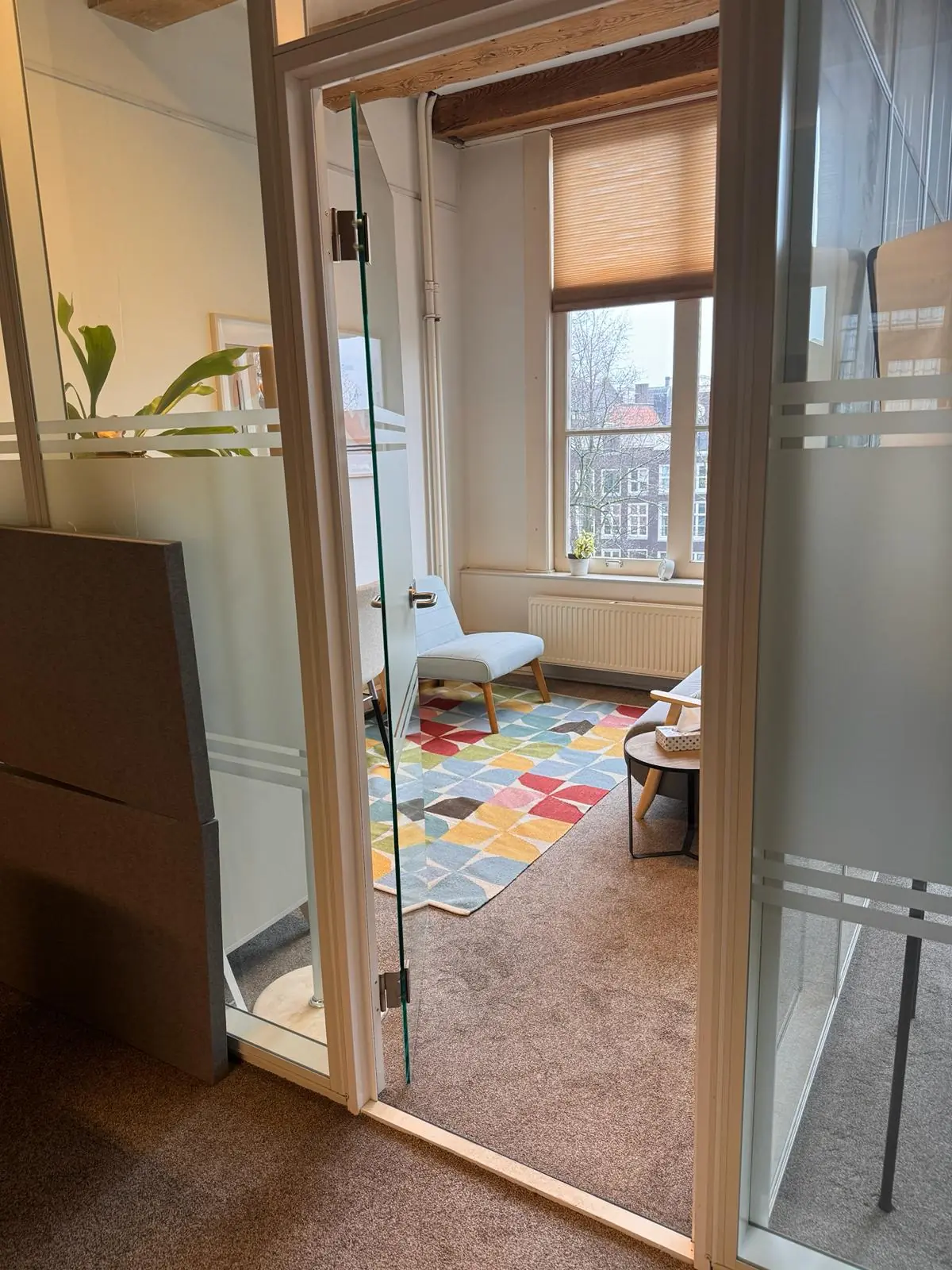 Doorkijk naar een sfeervol kantoor aan de Keizersgracht 241 met kleurrijk vloerkleed en grote raam met uitzicht.