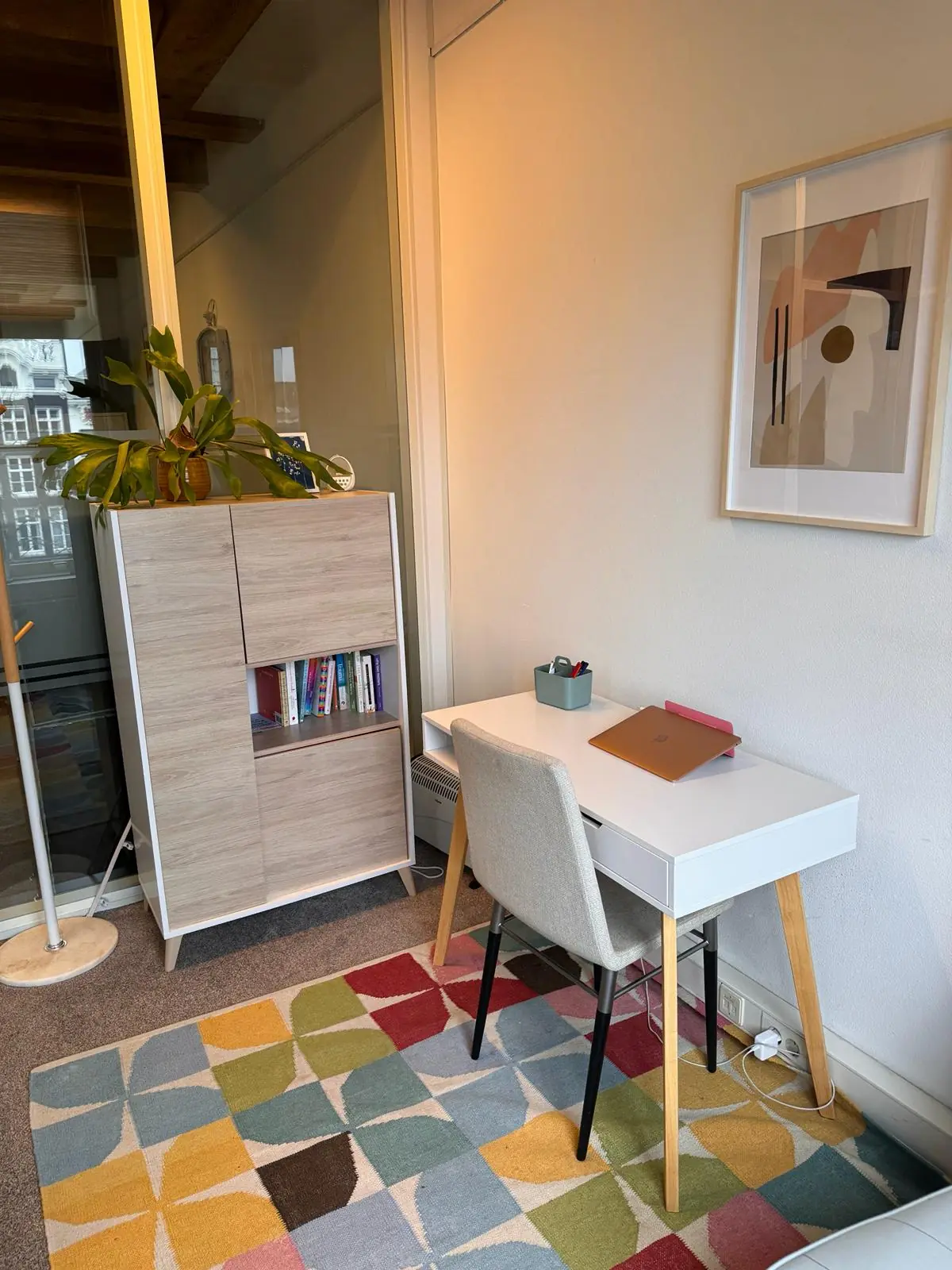 Klein thuiskantoor in Keizersgracht 241 met een bureau, stijlvolle kast, kleurrijk vloerkleed en abstracte wandkunst.