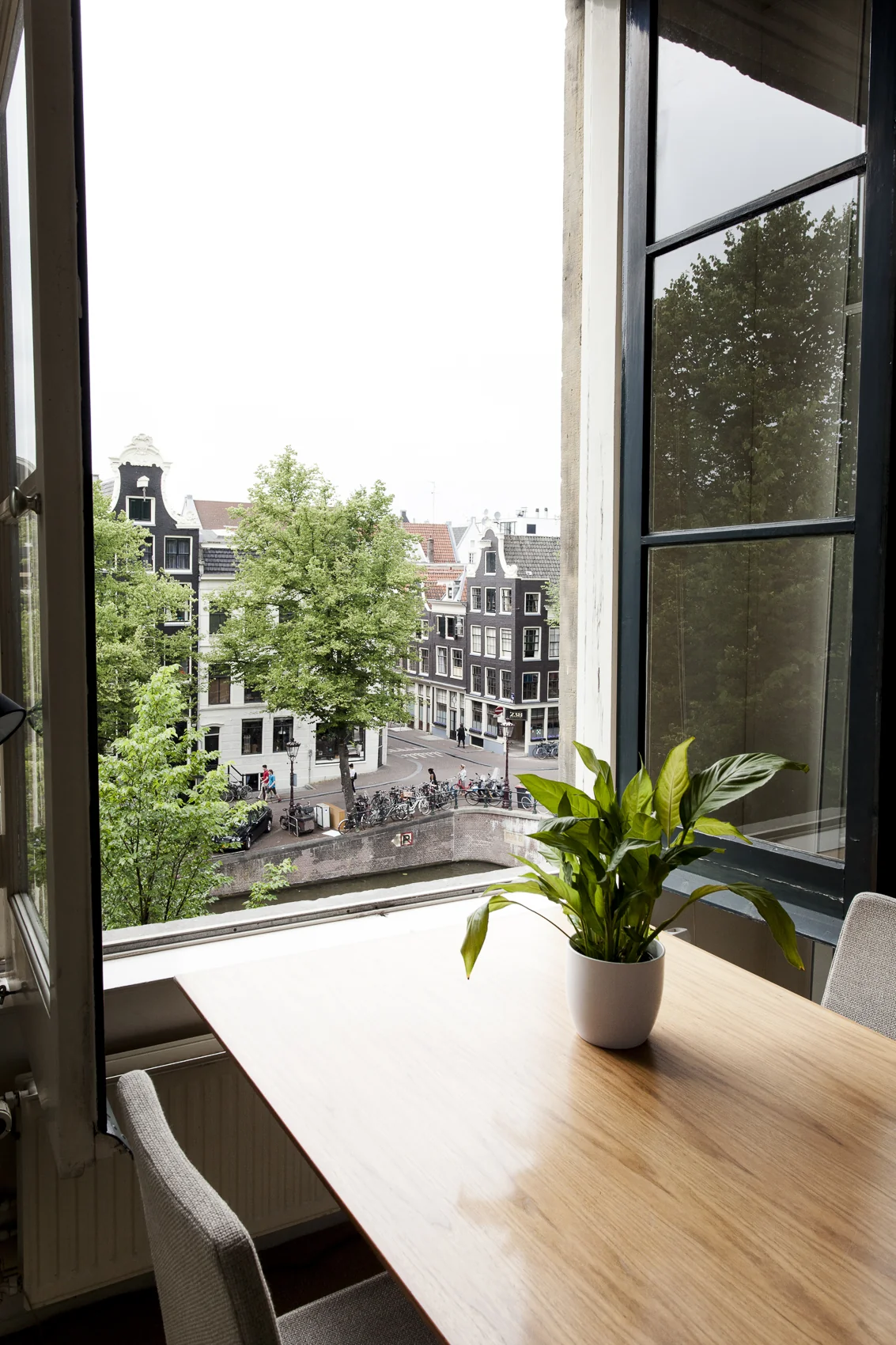 Vergadertafel met plant bij open raam met uitzicht op de Keizersgracht in Amsterdam.