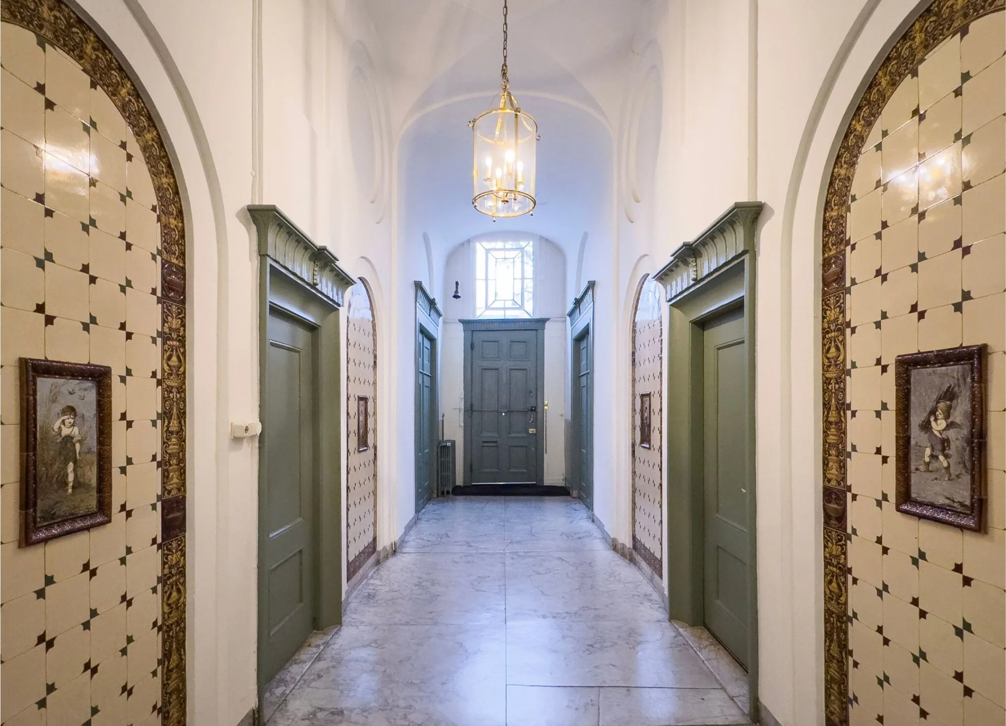 Gedeeltelijk betegelde gang in Keizersgracht 261 met groene deuren, klassieke schilderijen en een lantaarnvormige plafondlamp.