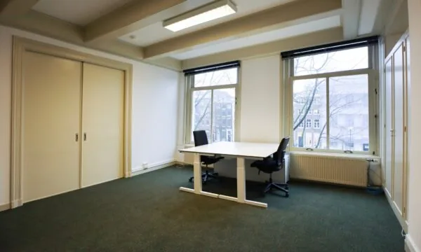 Kantoorruimte aan de Keizersgracht 261 met twee bureaustoelen, een bureau en uitzicht op de gracht.