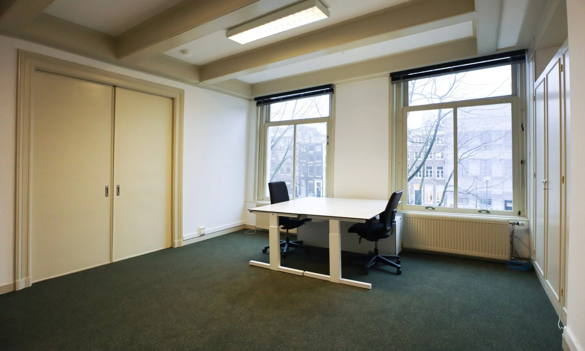 Kantoorruimte aan de Keizersgracht 261 met twee bureaustoelen, een bureau en uitzicht op de gracht.