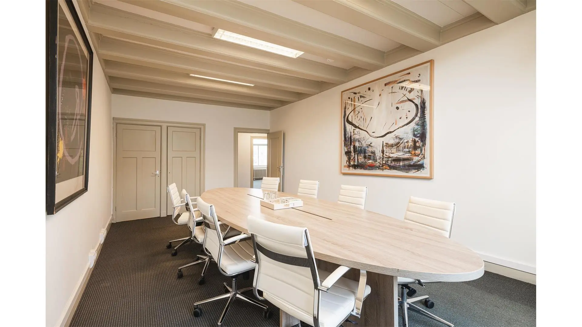 Vergaderruimte met ovale houten tafel, acht witte bureaustoelen en moderne kunst aan de muur in Keizersgracht 261.