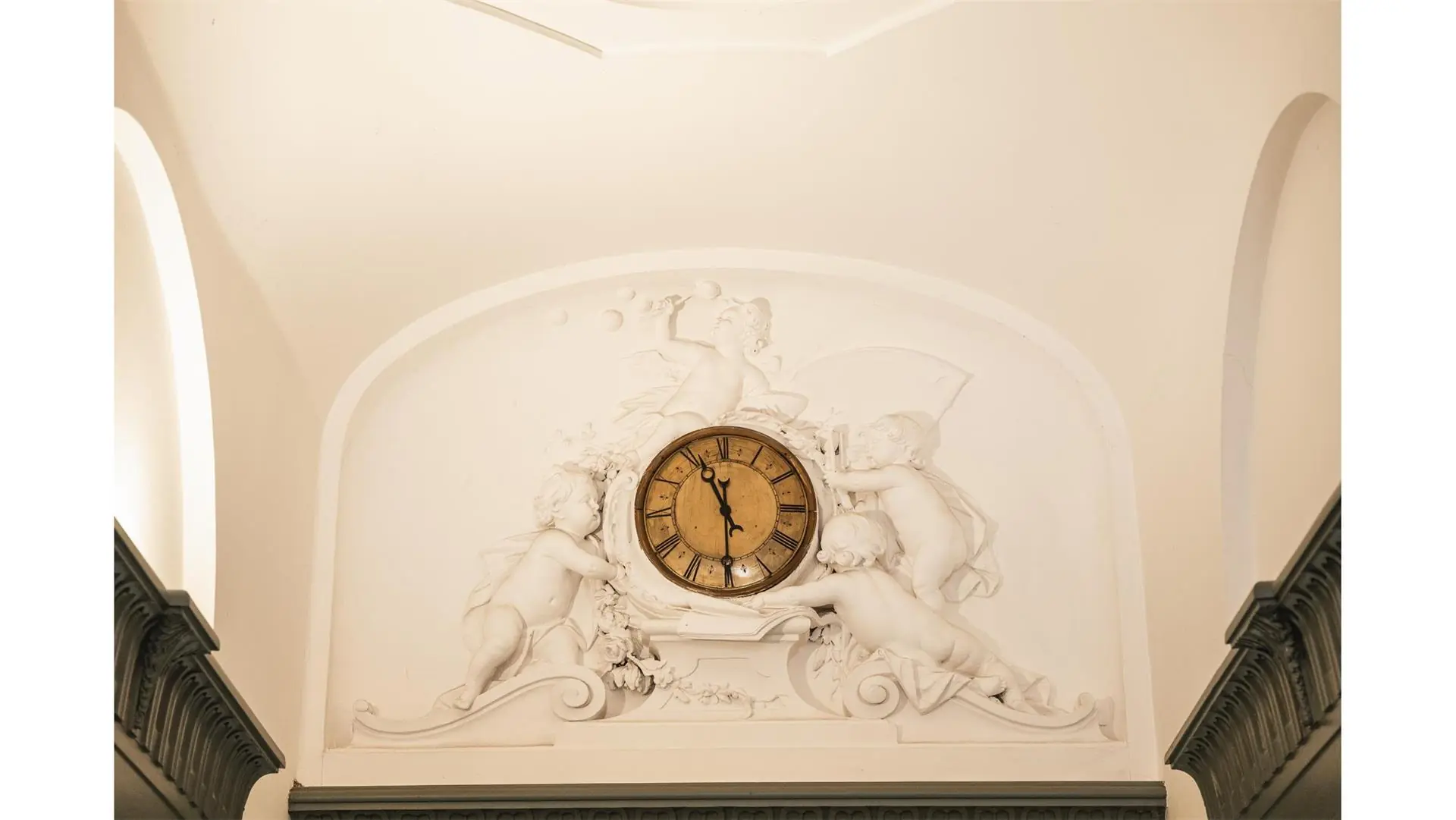 Houten klok omringd door wit stucwerk met spelende engelen in het interieur van Keizersgracht 261.