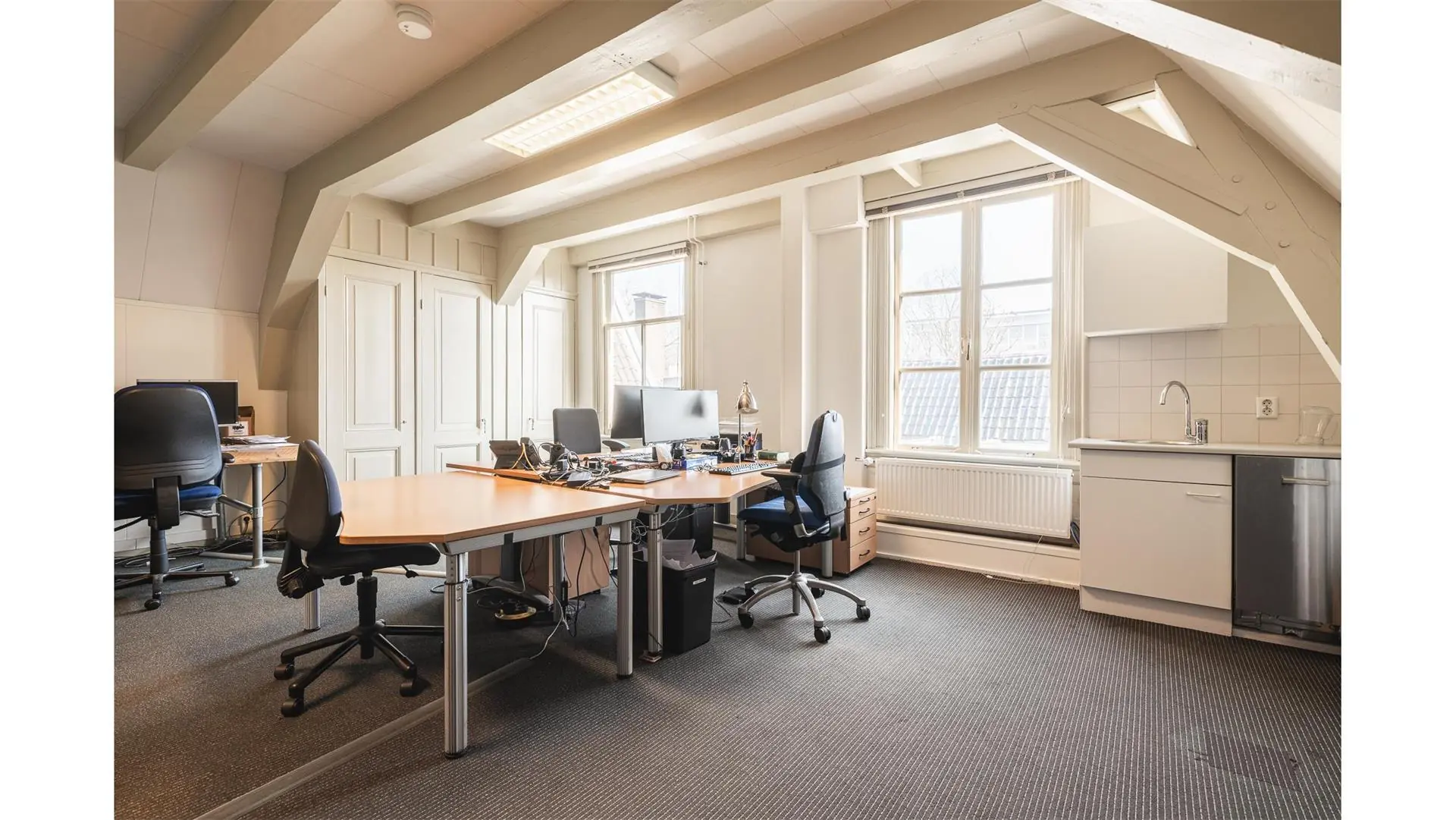 Kantoorruimte op Keizersgracht 261 met meerdere bureaus, bureaustoelen, computers en een kitchenette onder een schuine kap.