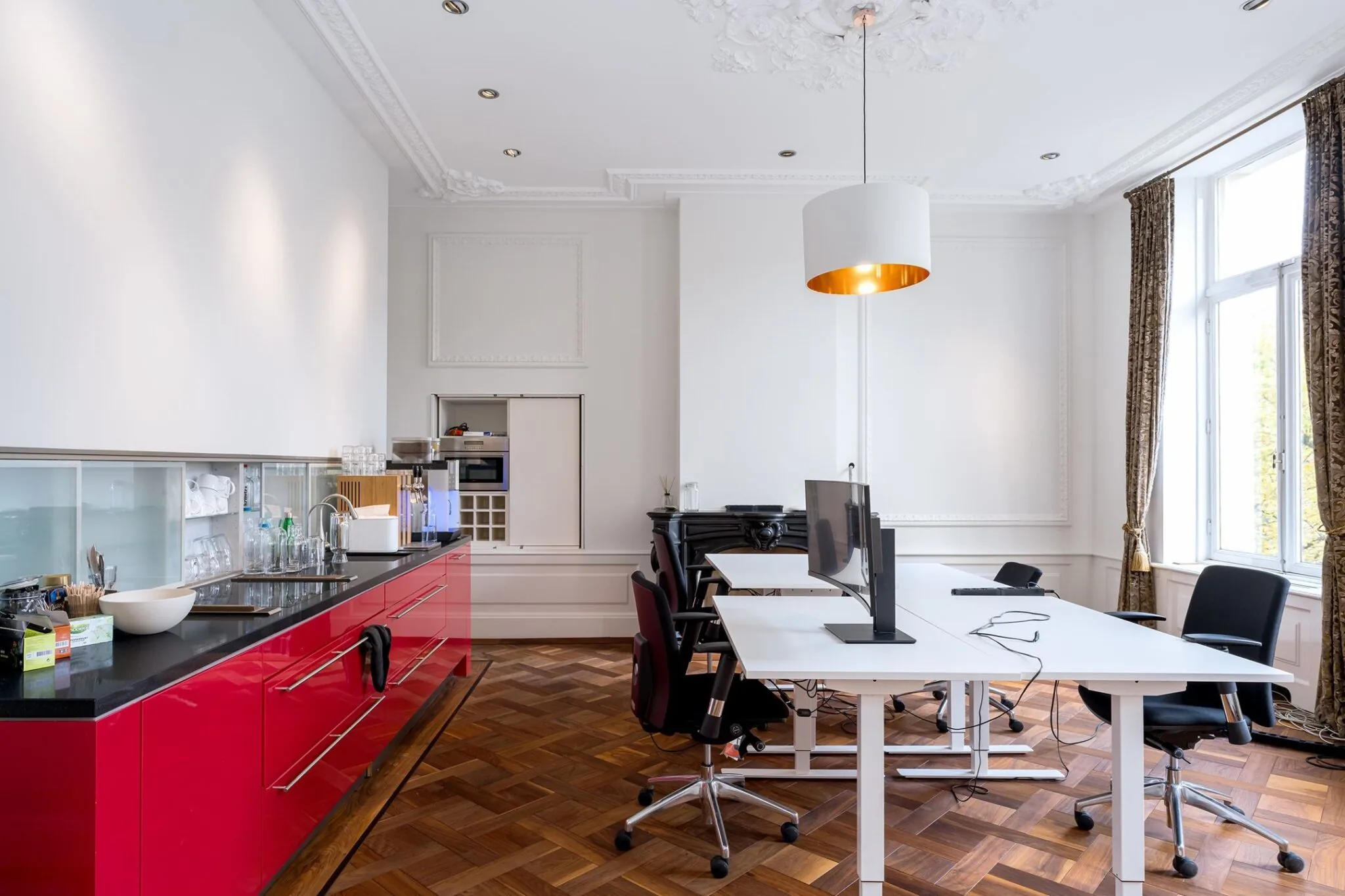 Kantoorruimte aan de Keizersgracht 452 met moderne werkplekken, een rode keuken en klassieke details zoals sierlijsten en een houten visgraatvloer.