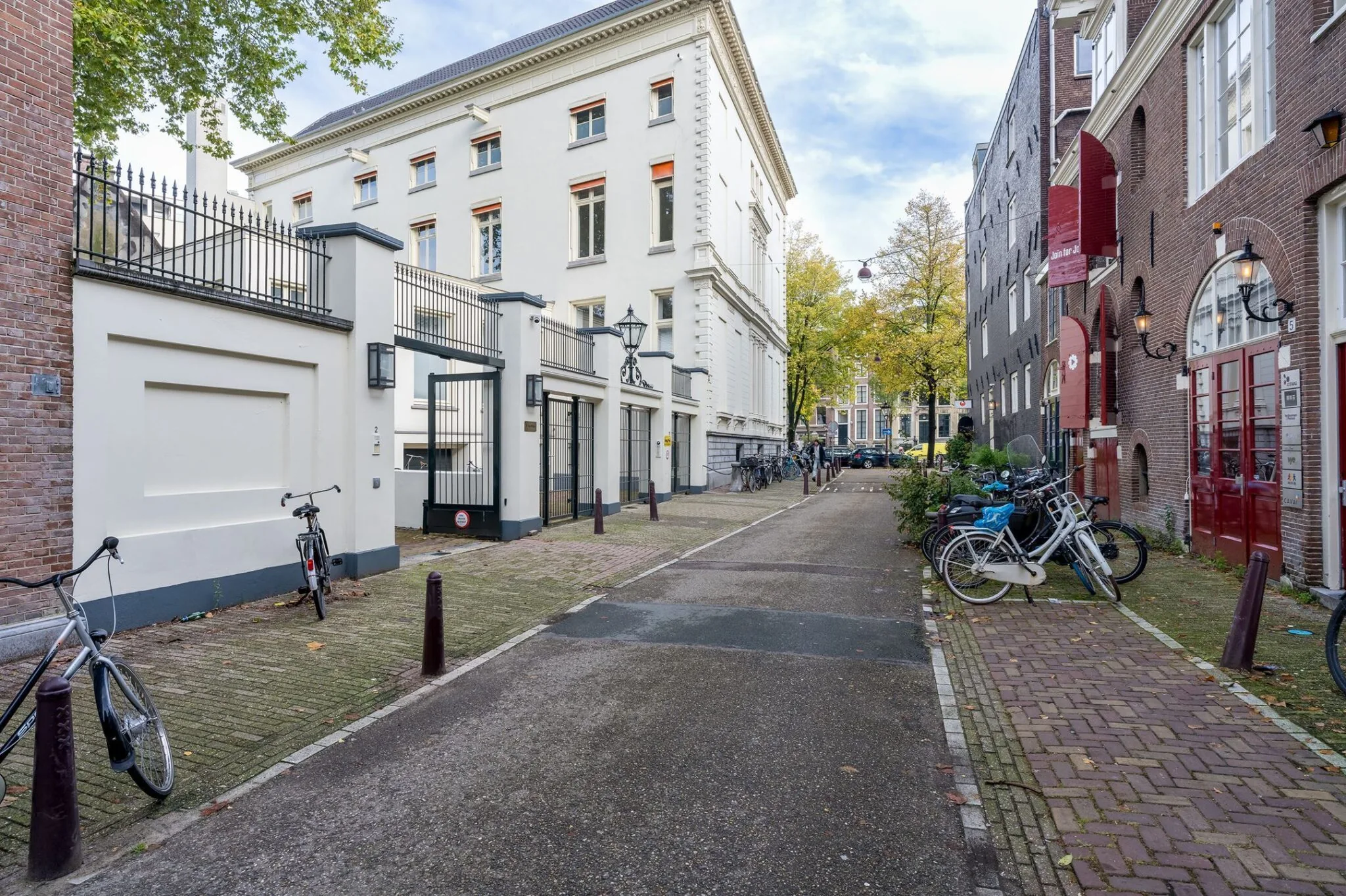 Straatbeeld van Keizersgracht 452 in Amsterdam met witte gevel, smeedijzeren hek en geparkeerde fietsen.