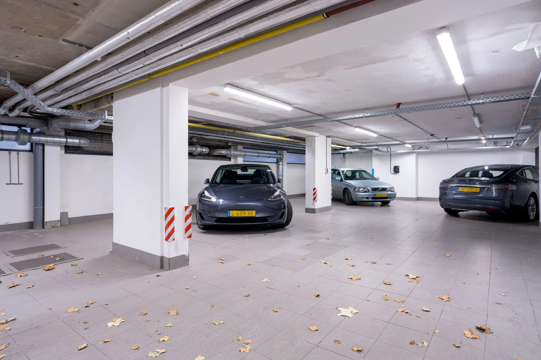 Ondergrondse parkeergarage bij Keizersgracht 452 met drie geparkeerde auto's en gevallen bladeren op de vloer.