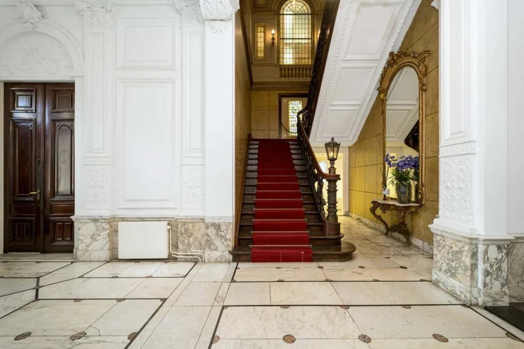 Monumentale hal van Keizersgracht 452 met een houten trap bekleed met rood tapijt, sierlijke details en een grote spiegel.