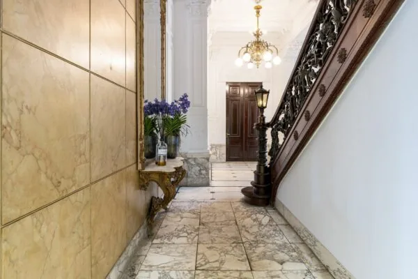 Luxe marmeren hal van Keizersgracht 452 met sierlijke houten trap, kroonluchter en bloemen op een vergulde console.